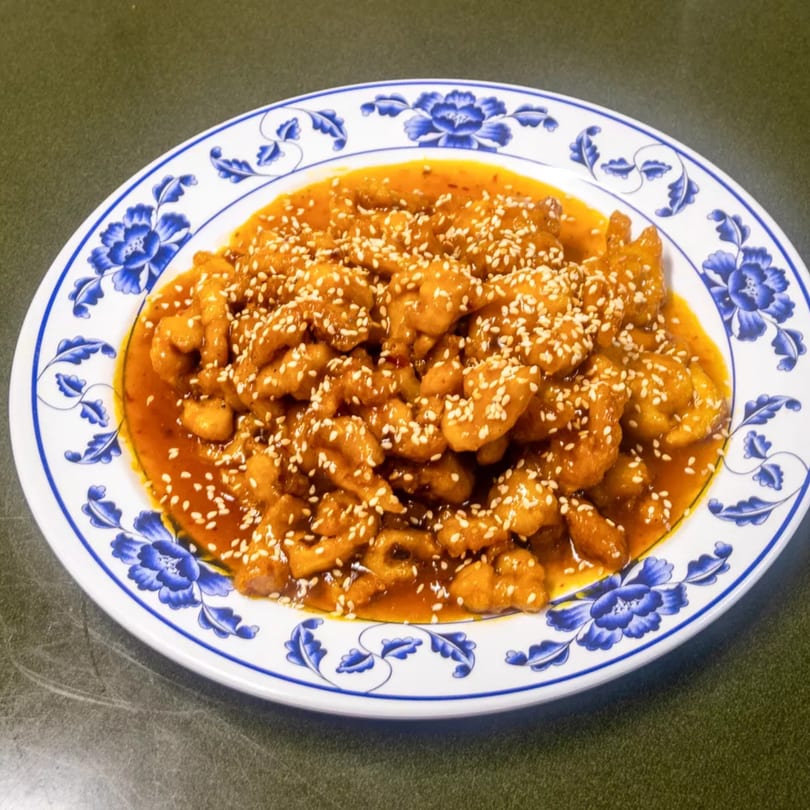 Sesame chicken in a rich orange sauce, sprinkled with sesame seeds, on a blue and white floral plate.