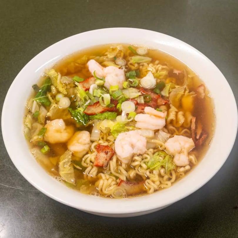 A white bowl of ramen with shrimp, pork, green onions, and cabbage in a clear broth.