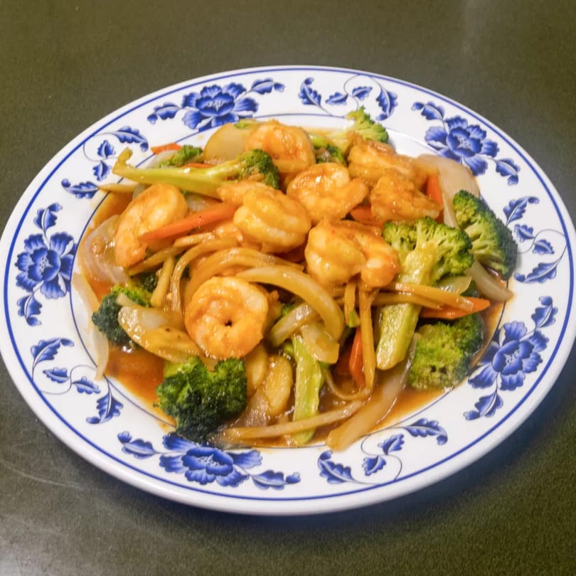 Shrimp stir-fry with broccoli, carrots, and onions in a savory sauce on a blue and white plate.