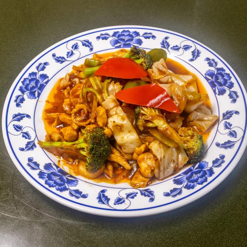 A colorful stir-fry with chicken, broccoli, red bell peppers, and other vegetables on a blue and white plate.