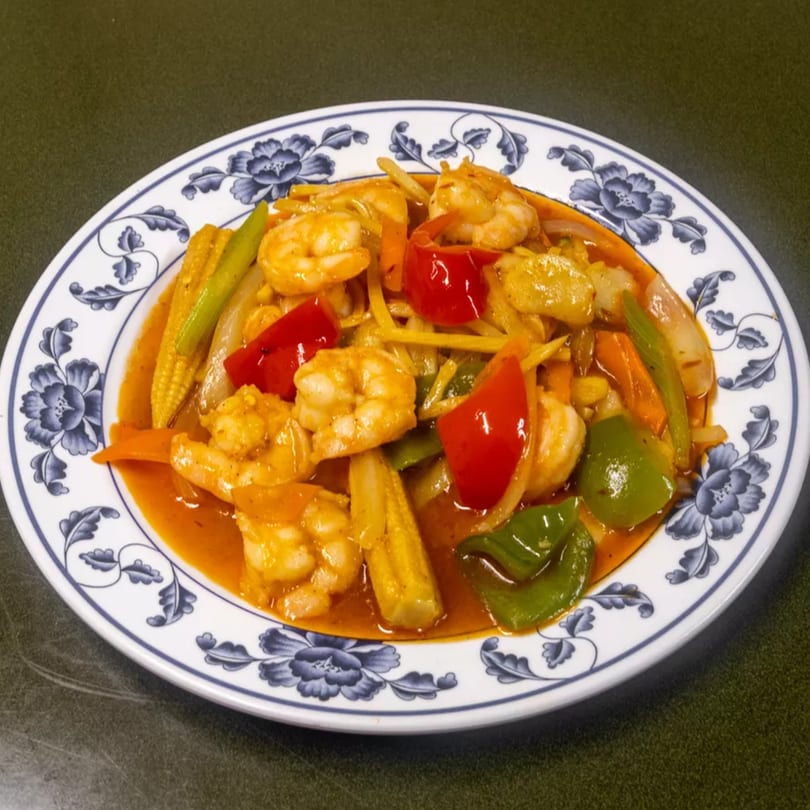 Shrimp stir-fry with baby corn, bell peppers, and onions in a rich orange sauce on a white plate.