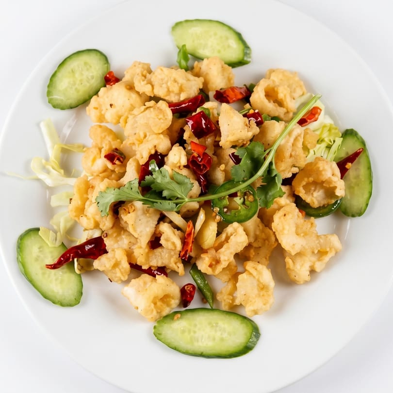 Crispy fried calamari with red chili peppers, cilantro, jalapeños, and cucumber slices on a white plate.