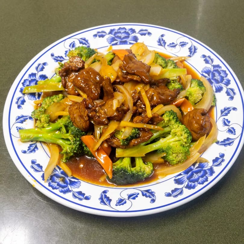 Beef and broccoli stir-fry with onions and carrots in a rich brown sauce on a floral plate.